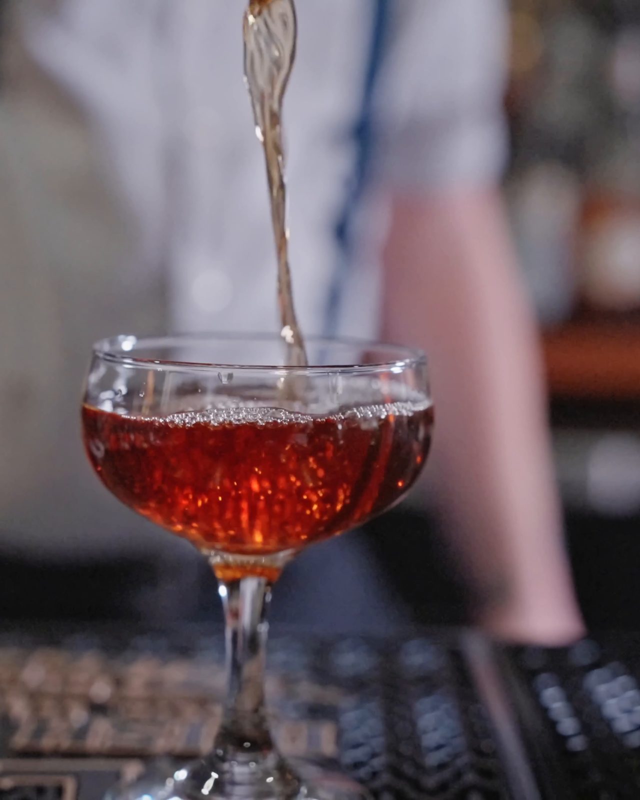 A red cocktail poured into a coupe at the bar